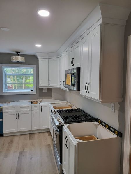 White kitchen cabinets with black hardware installed, unfinished countertops, and wood-look flooring.