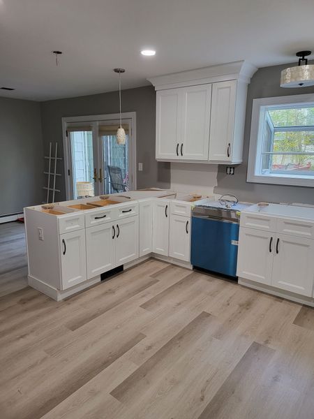 White kitchen with new cabinets, a blue dishwasher, and light wood flooring.