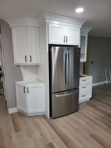 White kitchen cabinets with black handles frame a stainless steel refrigerator.