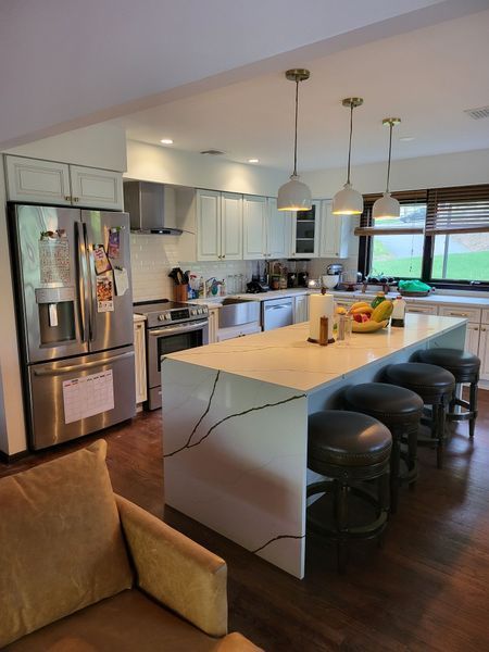 Modern kitchen with white cabinets, island, and stainless steel appliances; stools at island.