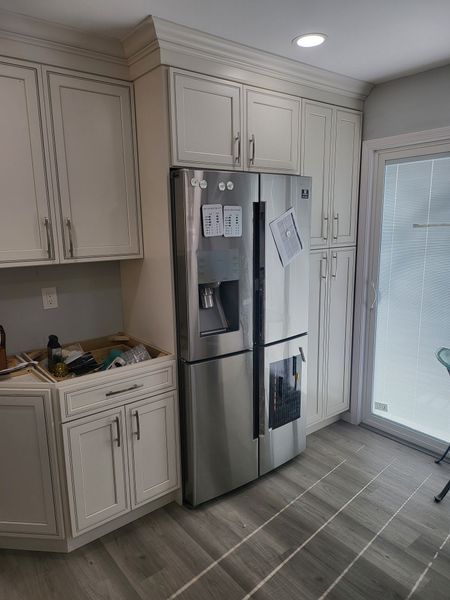 Kitchen with stainless steel refrigerator, white cabinets, and gray wood-look flooring. A sliding glass door is on the right.