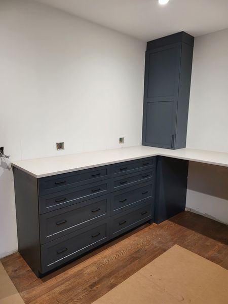 Dark blue kitchen cabinets with white countertop and tall matching cabinet on the right.