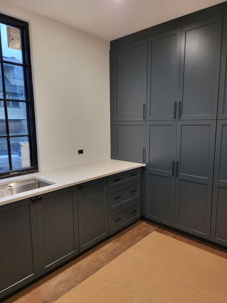Dark gray cabinets in a corner of a room, with a countertop and window.