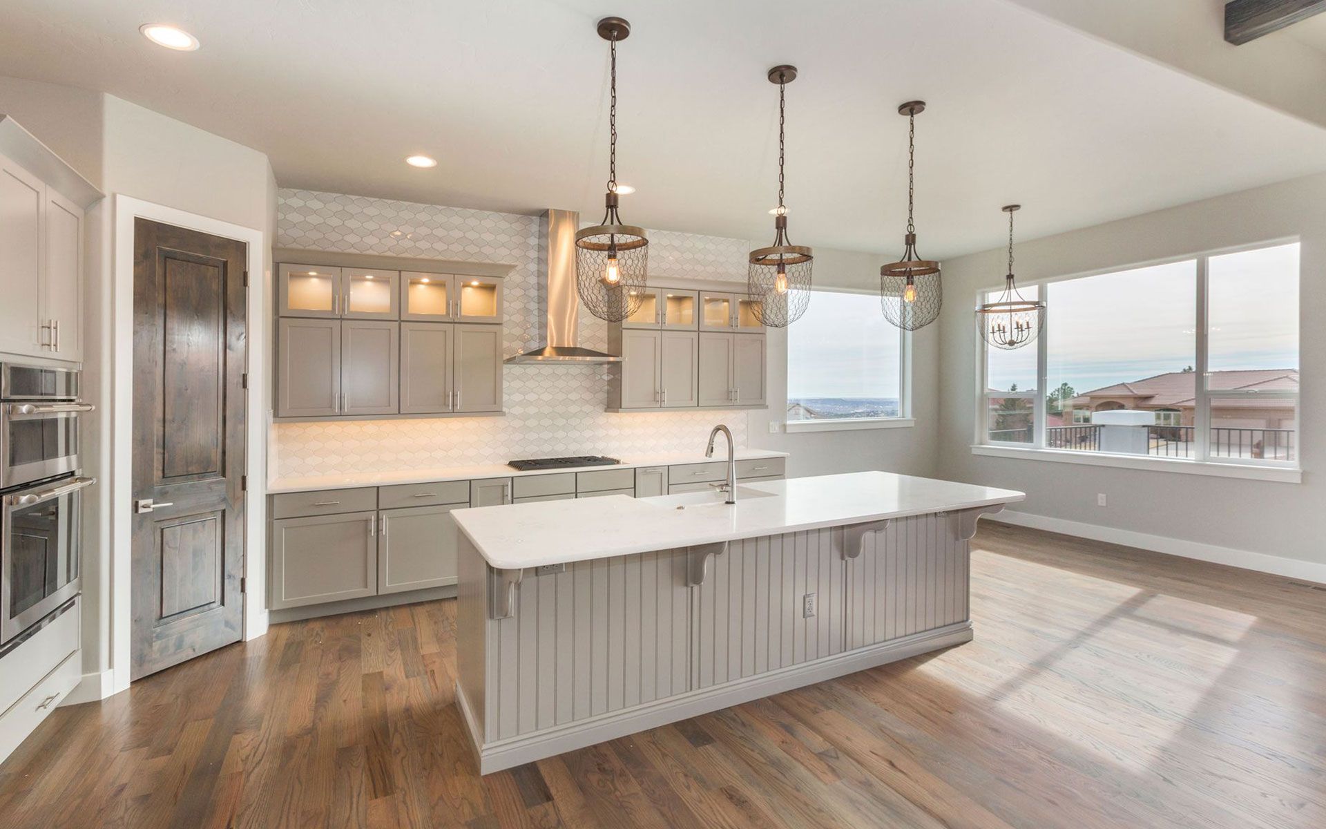 Modern kitchen with a gray island, light cabinets, and large windows.