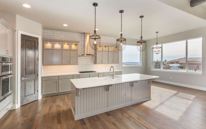 Modern kitchen with island, gray cabinets, stainless steel appliances, and large windows.