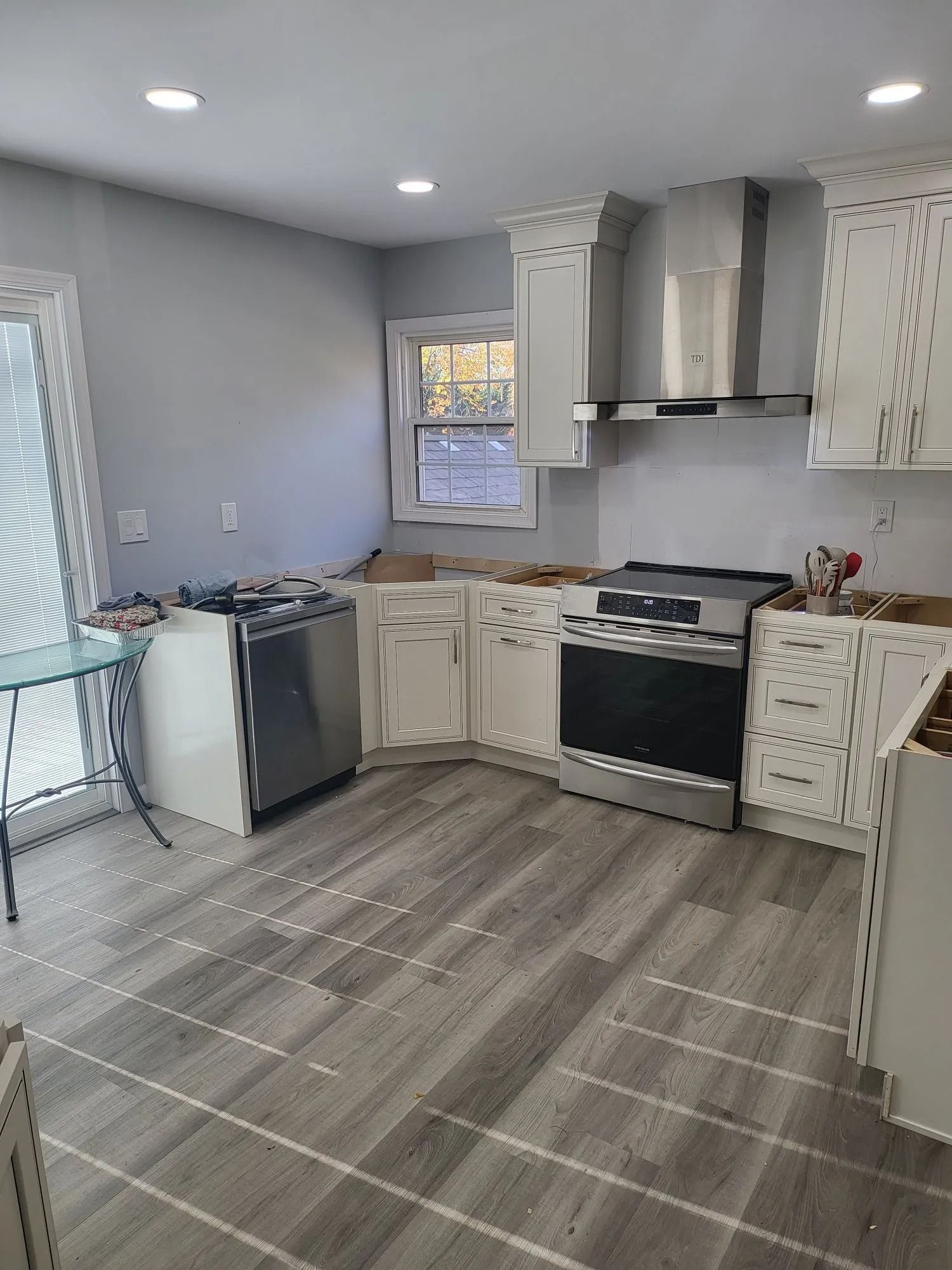 Kitchen renovation with gray tile floor, white cabinets, and stainless steel appliances.