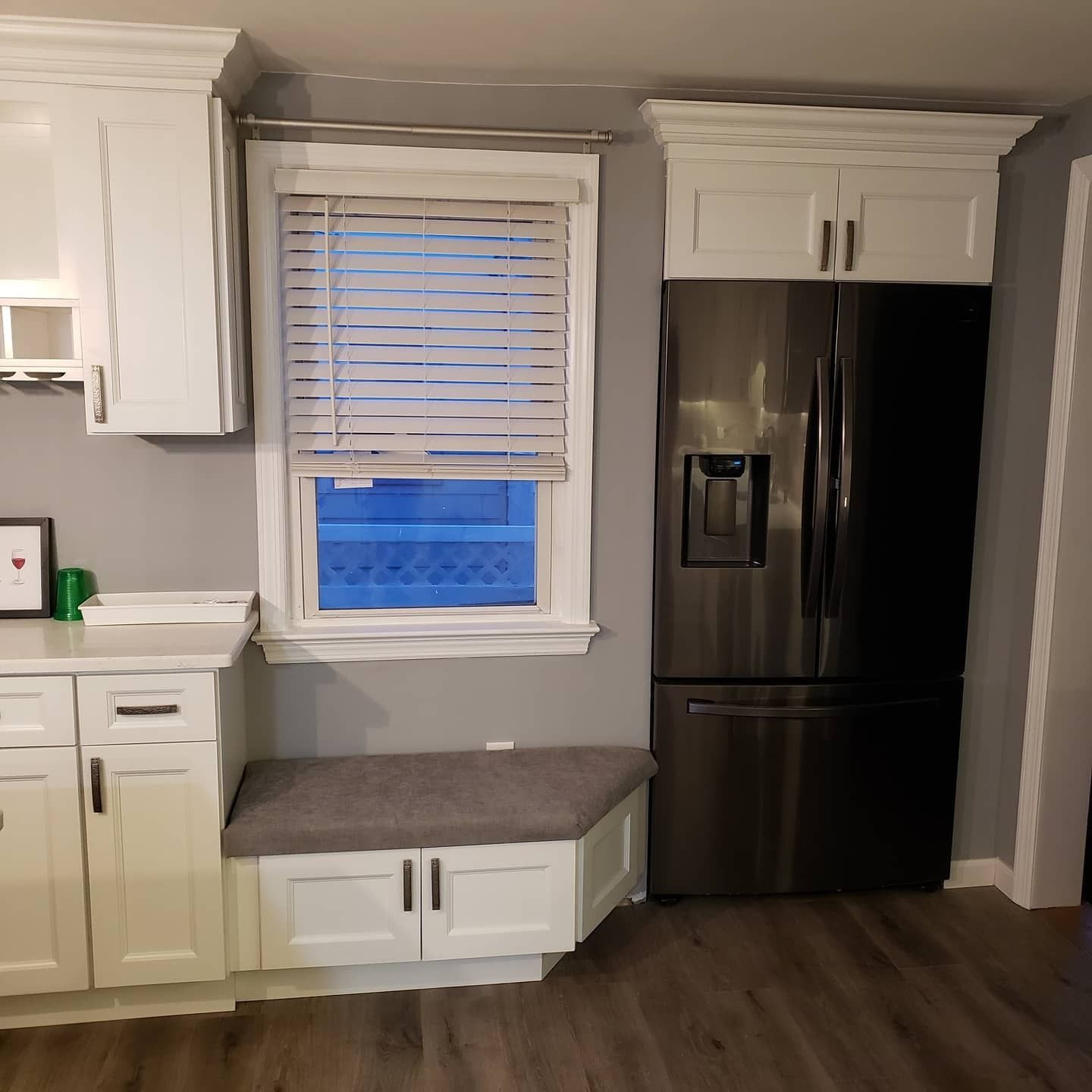 Kitchen with white cabinets, stainless steel refrigerator, and window seat with blinds.