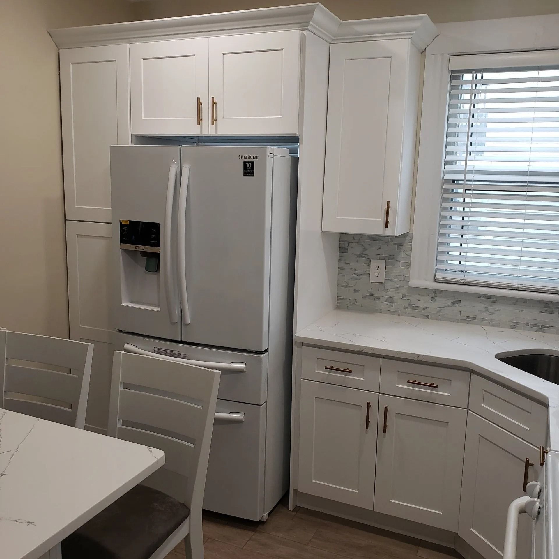 White kitchen with cabinets, refrigerator, and a window with blinds.