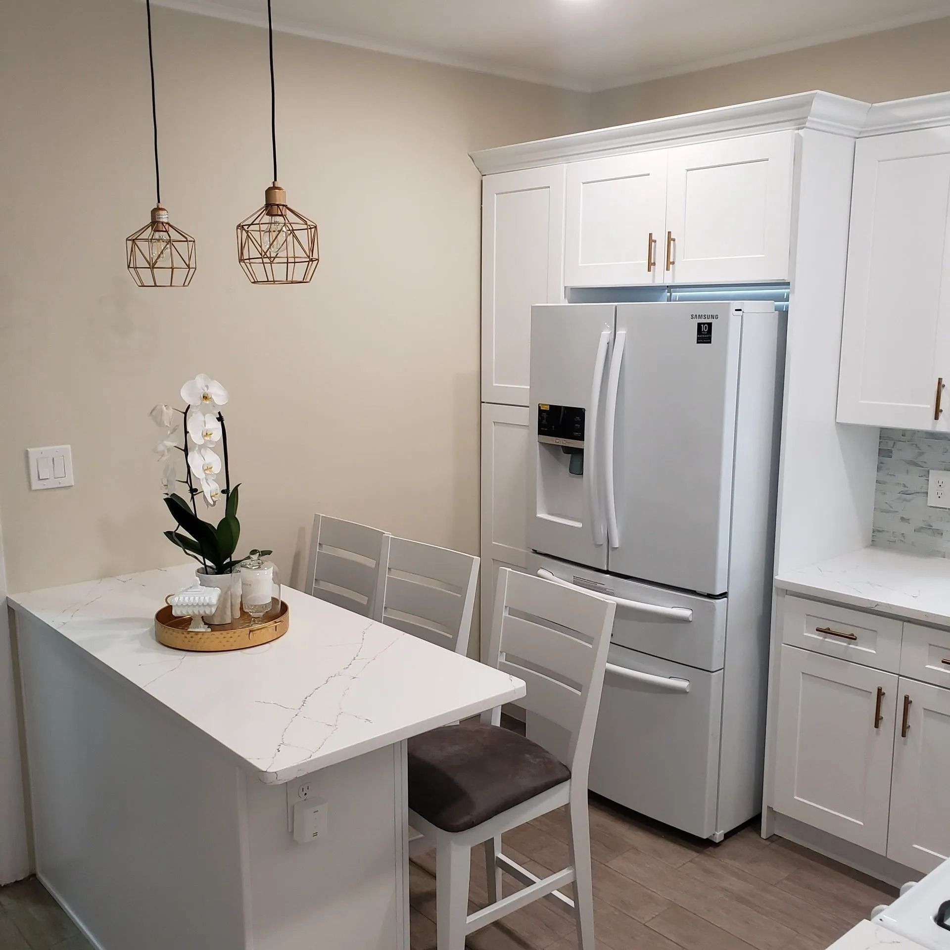 White kitchen with a breakfast bar, white appliances, and hanging lights.