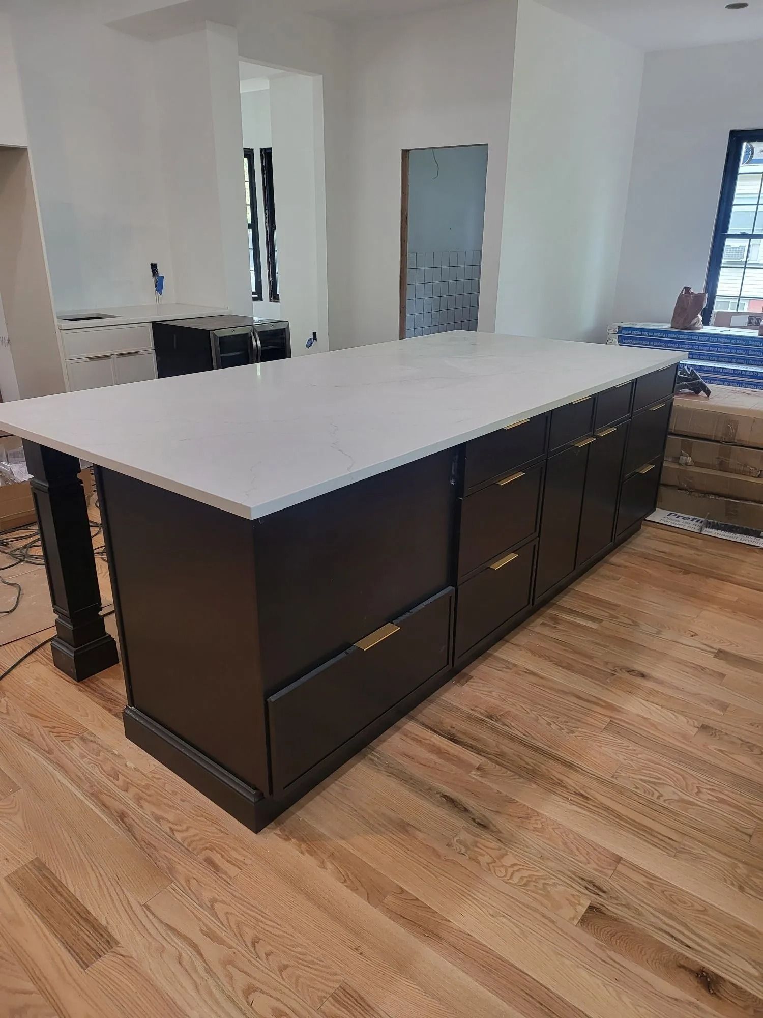 Black kitchen island with a white countertop and gold hardware on hardwood floors.