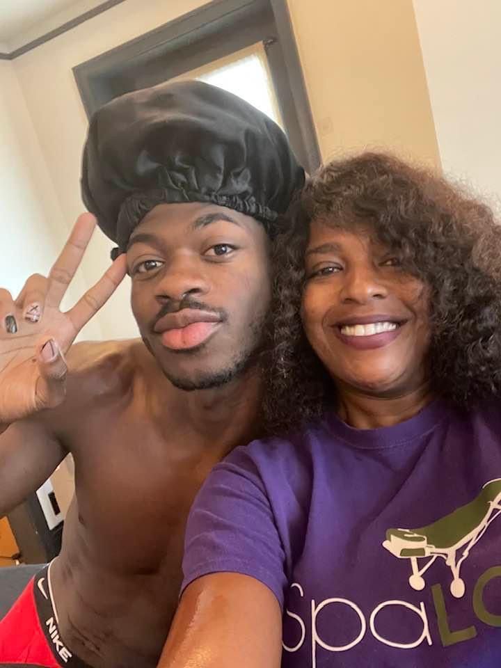 A woman in a purple shirt is standing next to a shirtless man in a black hat.