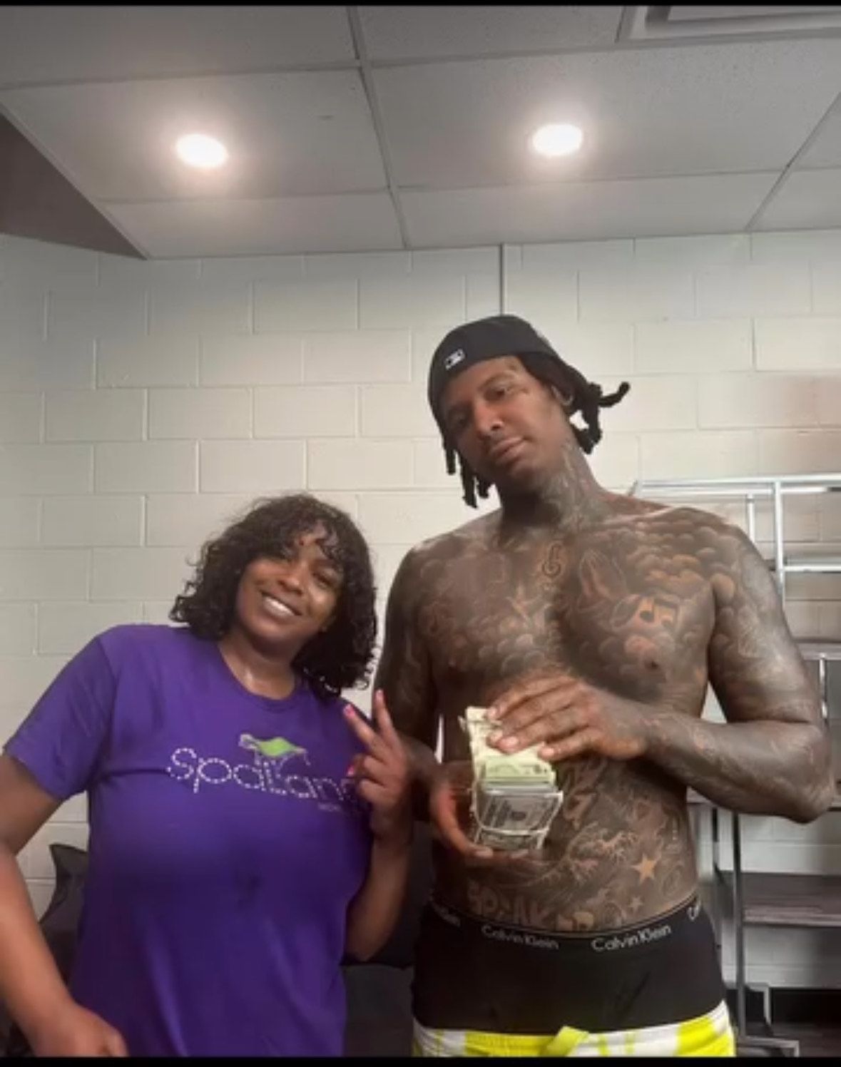 A woman in a purple shirt stands next to a shirtless man holding money