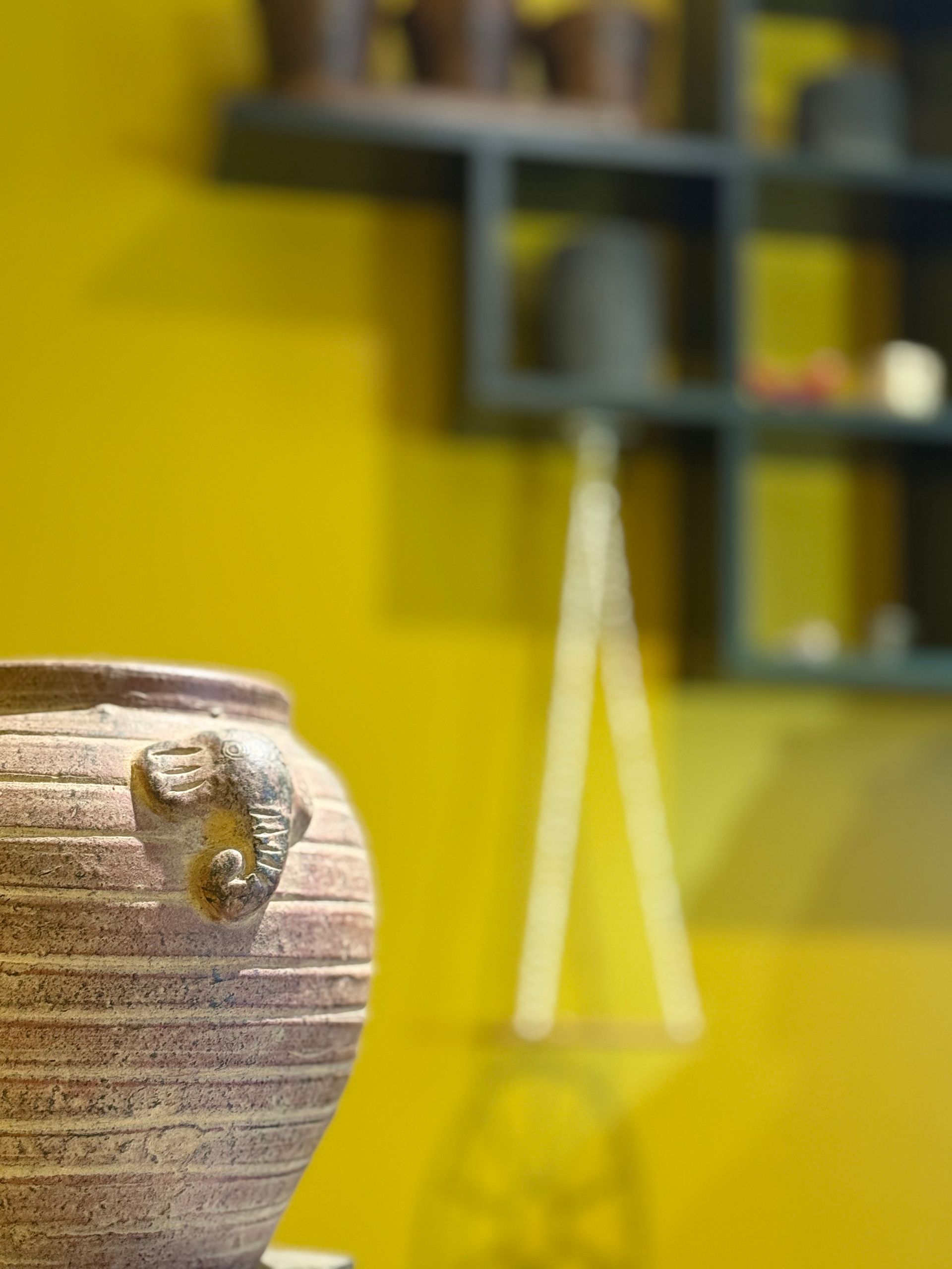 A vase with a handle is sitting in front of a yellow wall