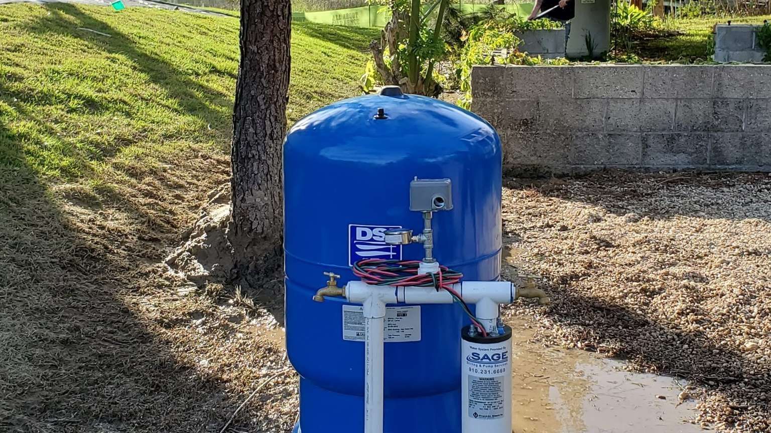 a blue water tank with a faucet attached to it is sitting next to a tree