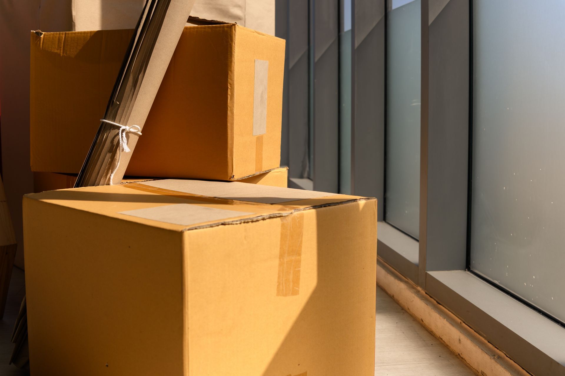 Stacked cardboard boxes by a window with a broom leaning against them