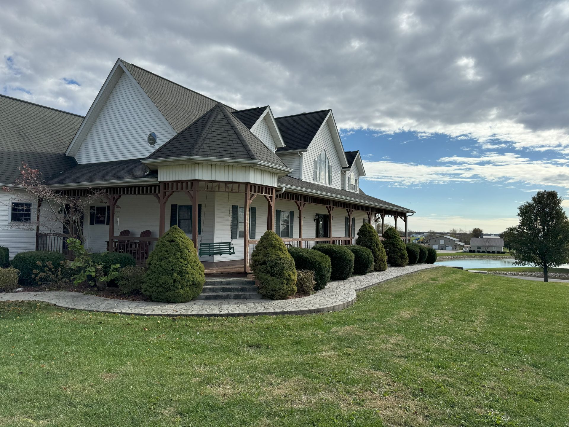 A large white house with a porch is sitting on top of a lush green hill.