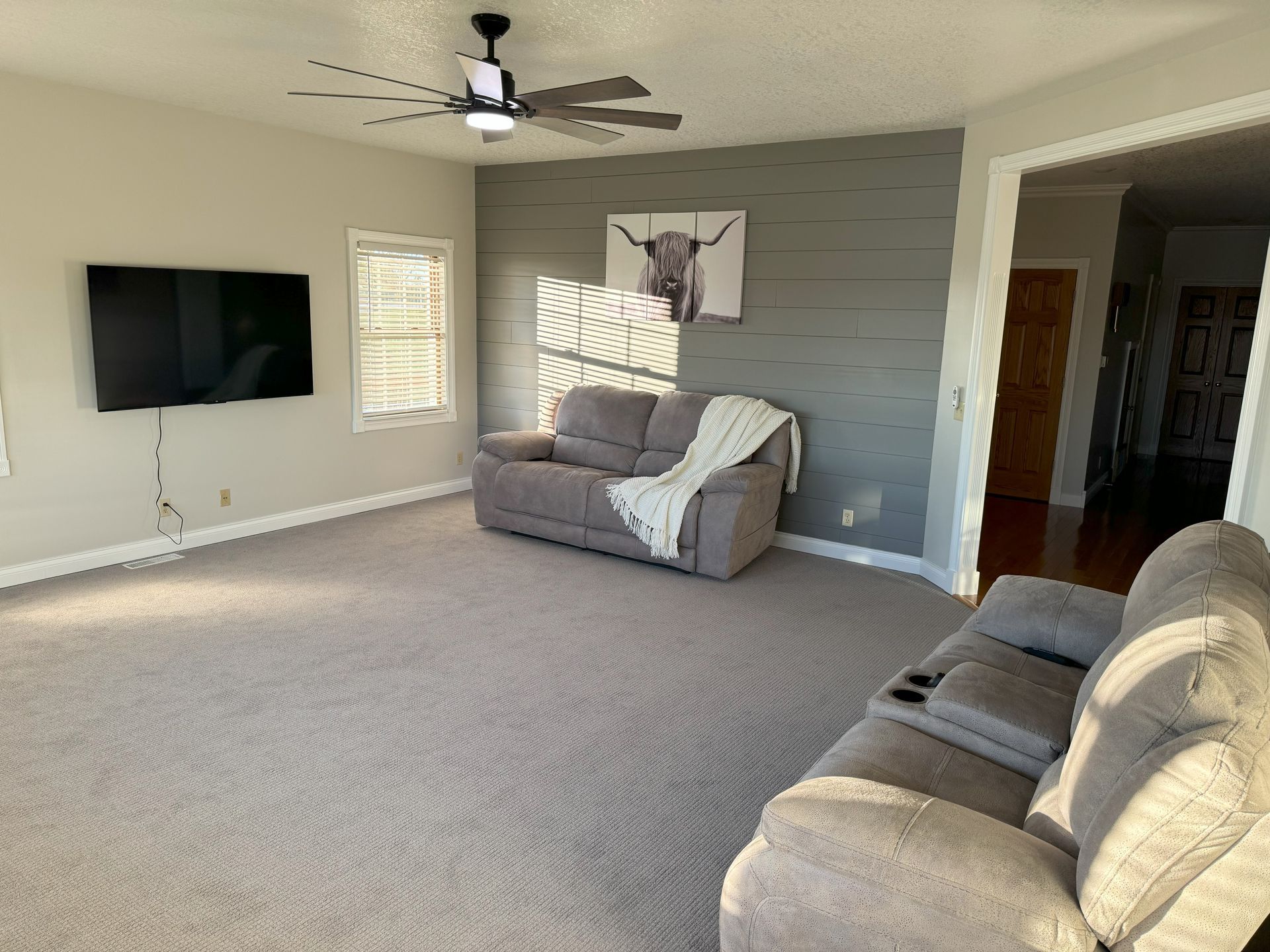 A living room with a couch , chair , television and ceiling fan.