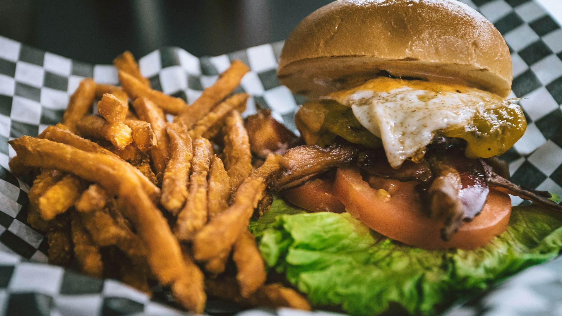 A close up of a hamburger and french fries on a checkered paper.