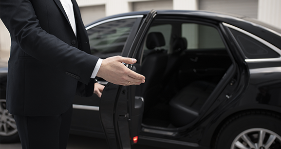 A man is holding an umbrella over a woman getting out of a car.