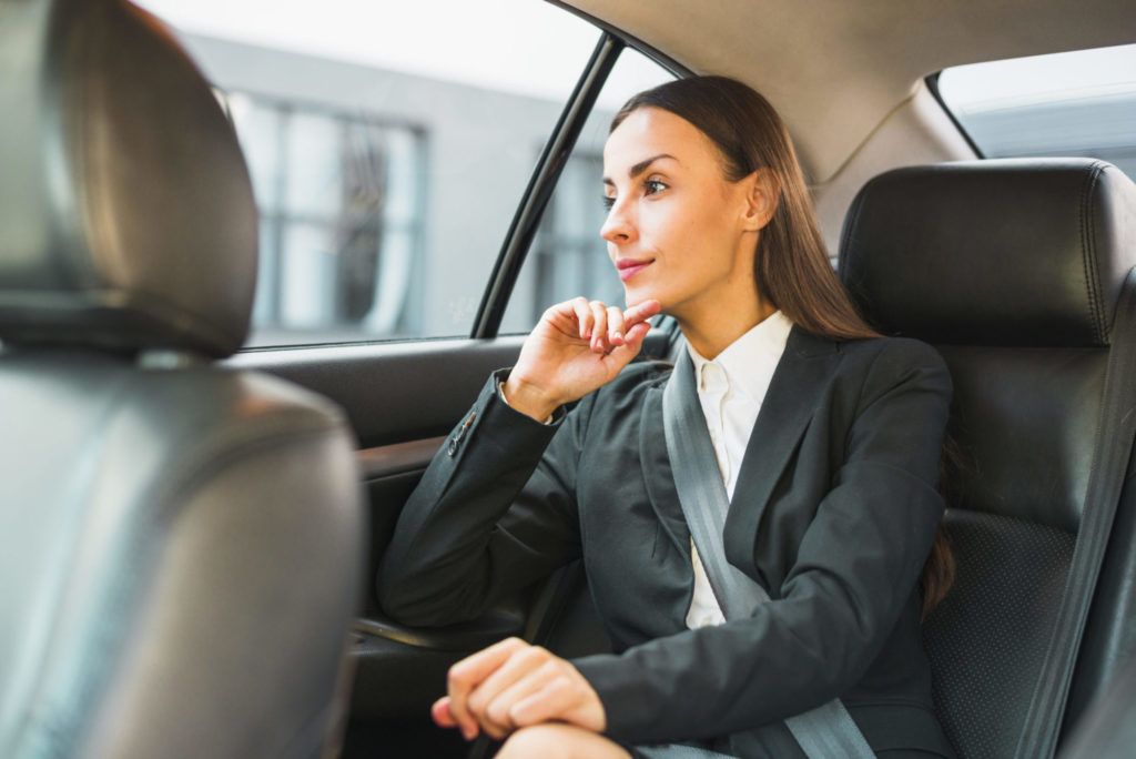 A woman in a suit is sitting in the back seat of a car.