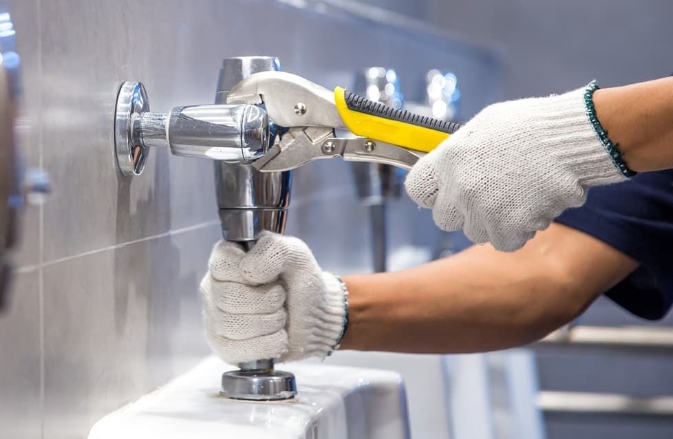 A Man Is Fixing A Toilet With A Wrench In A Bathroom — JSB Plumbing & Gas In South Grafton, NSW