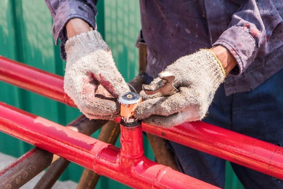 A Man Wearing Gloves Is Working On A Red Pipe — JSB Plumbing & Gas In South Grafton, NSW