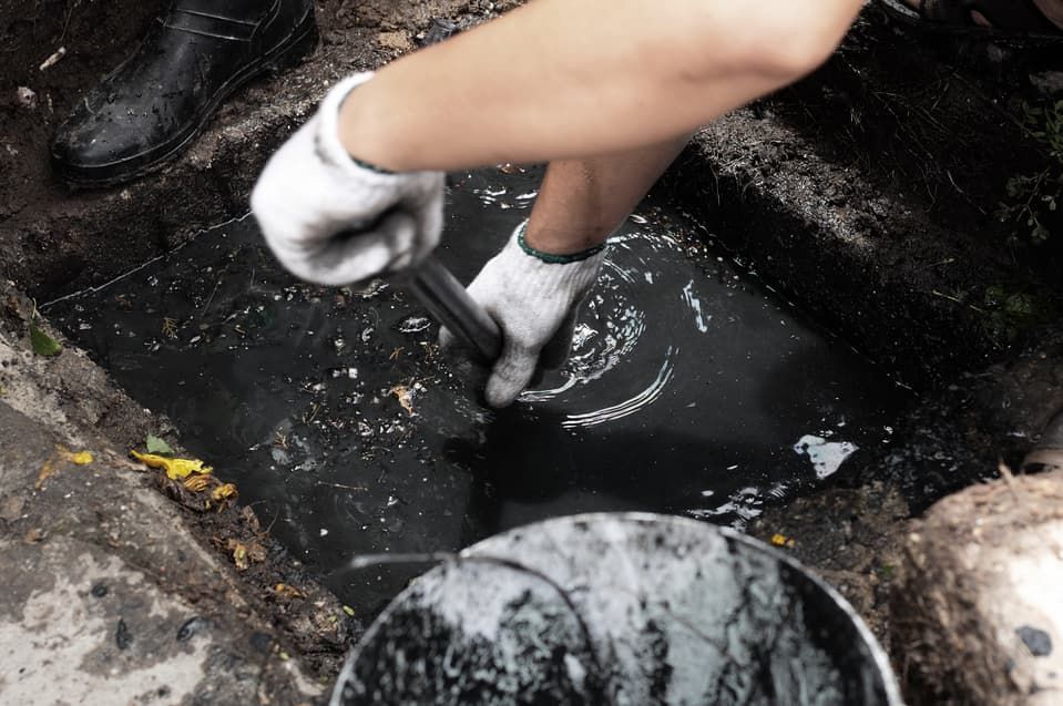 A Person Is Cleaning A Drain With A Shovel And A Bucket — JSB Plumbing & Gas In South Grafton, NSW