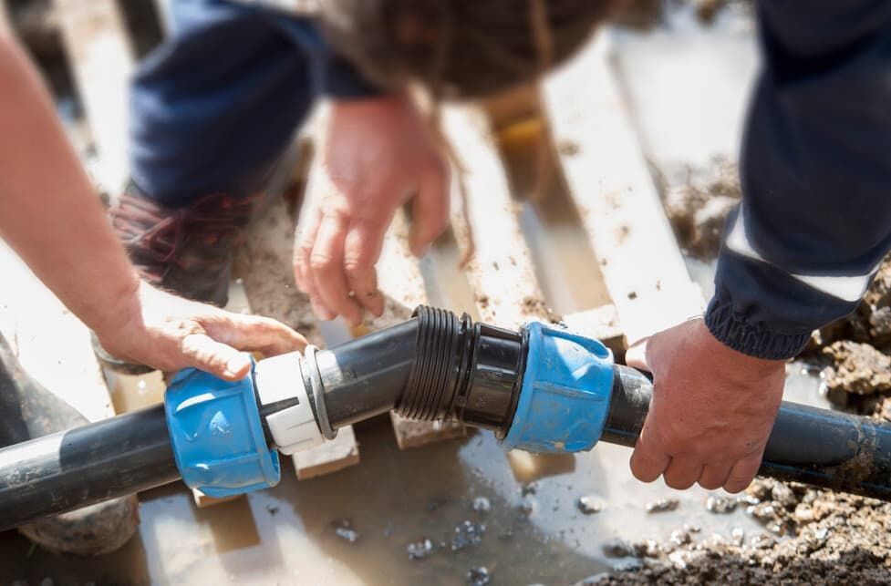 A Man Is Fixing A Water Pipe In The Mud — JSB Plumbing & Gas In South Grafton, NSW