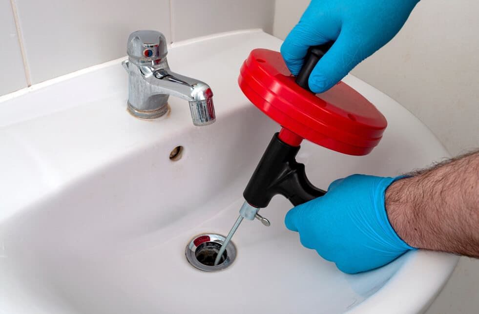 A Person Is Using A Drain Snake To Unblock A Sink — JSB Plumbing & Gas In South Grafton, NSW