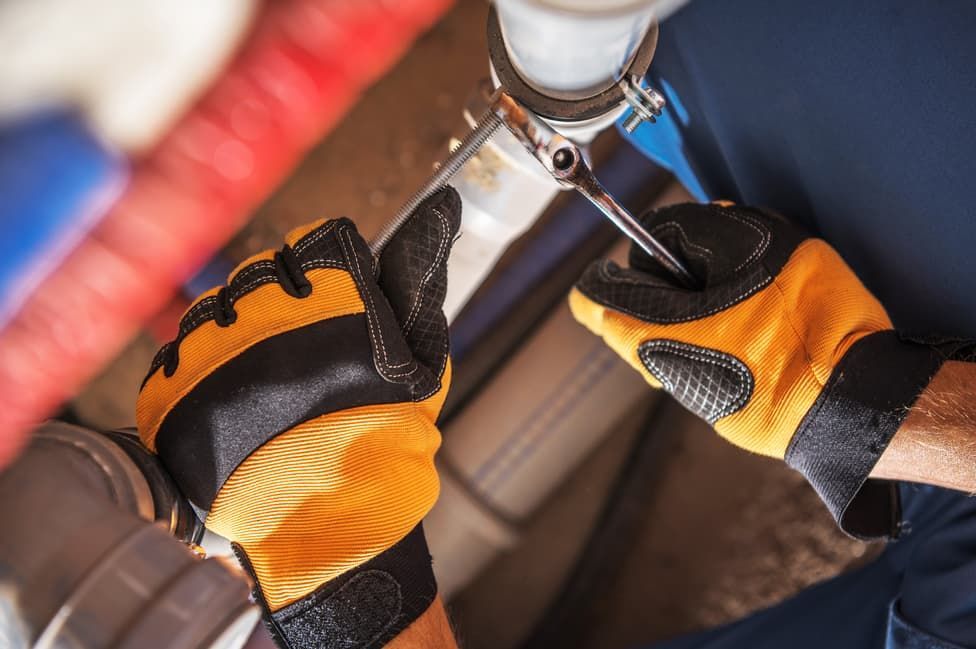 A Man Wearing Yellow Gloves Is Fixing A Pipe With A Wrench — JSB Plumbing & Gas In South Grafton, NSW
