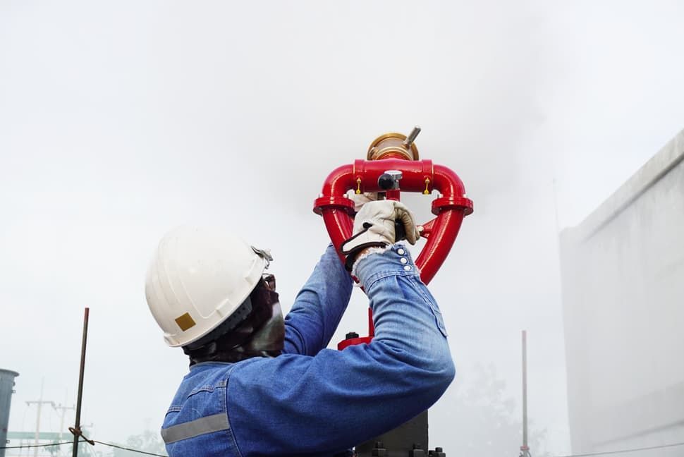 A Man In A Hard Hat Is Working On A Red Pipe — JSB Plumbing & Gas In South Grafton, NSW