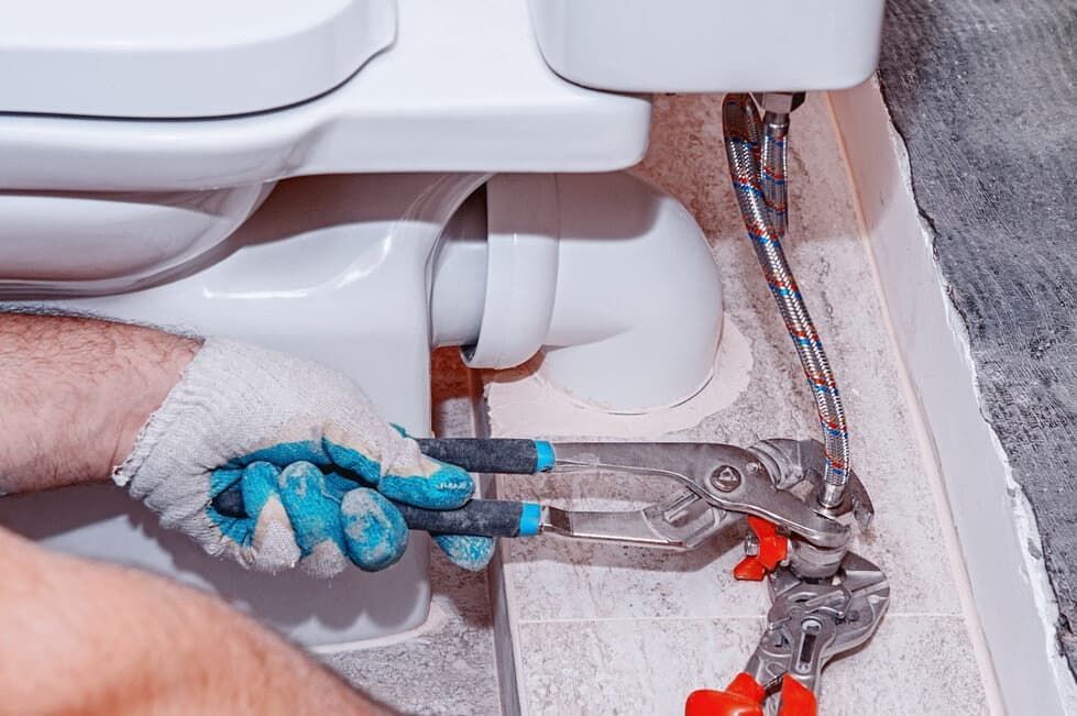 A Man Is Fixing A Toilet With A Pair Of Pliers — JSB Plumbing & Gas In South Grafton, NSW