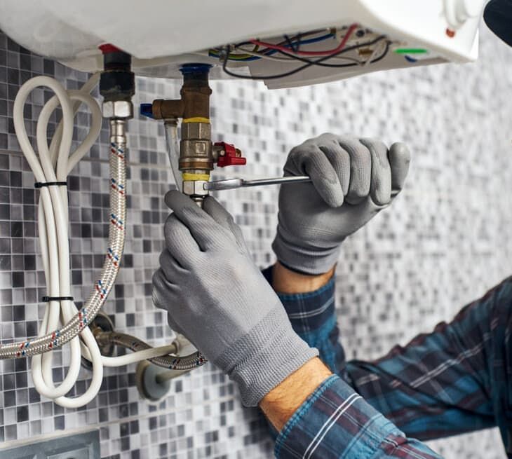 A Man Is Fixing A Water Heater With A Screwdriver — JSB Plumbing & Gas In South Grafton, NSW