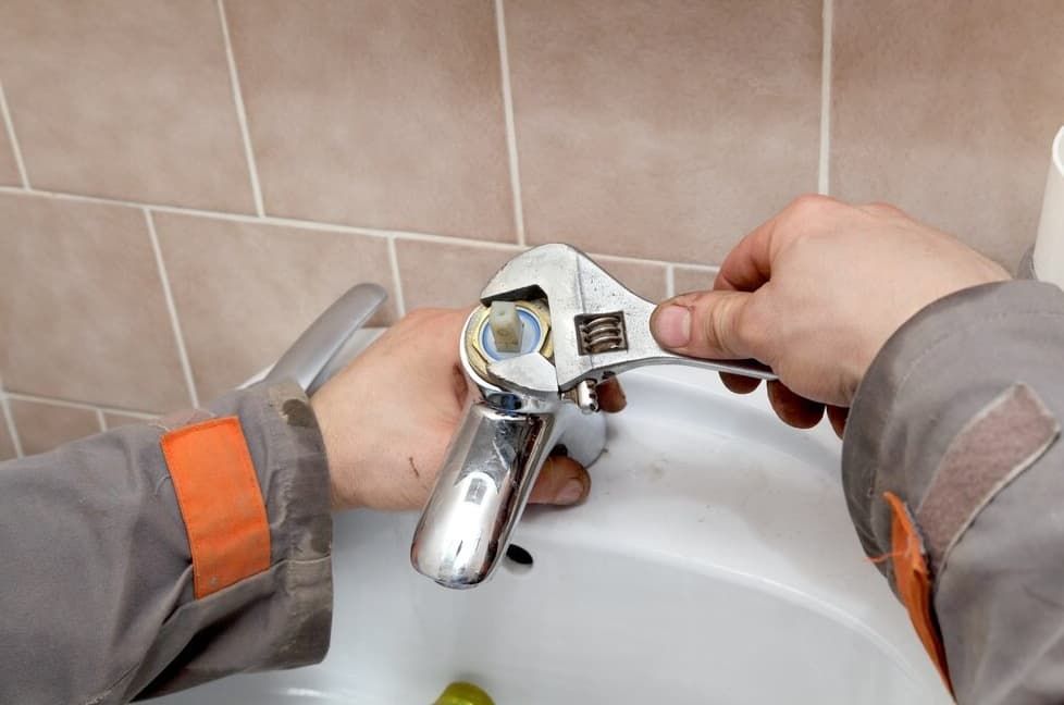 A Person Is Fixing A Sink Faucet With A Wrench — JSB Plumbing & Gas In South Grafton, NSW