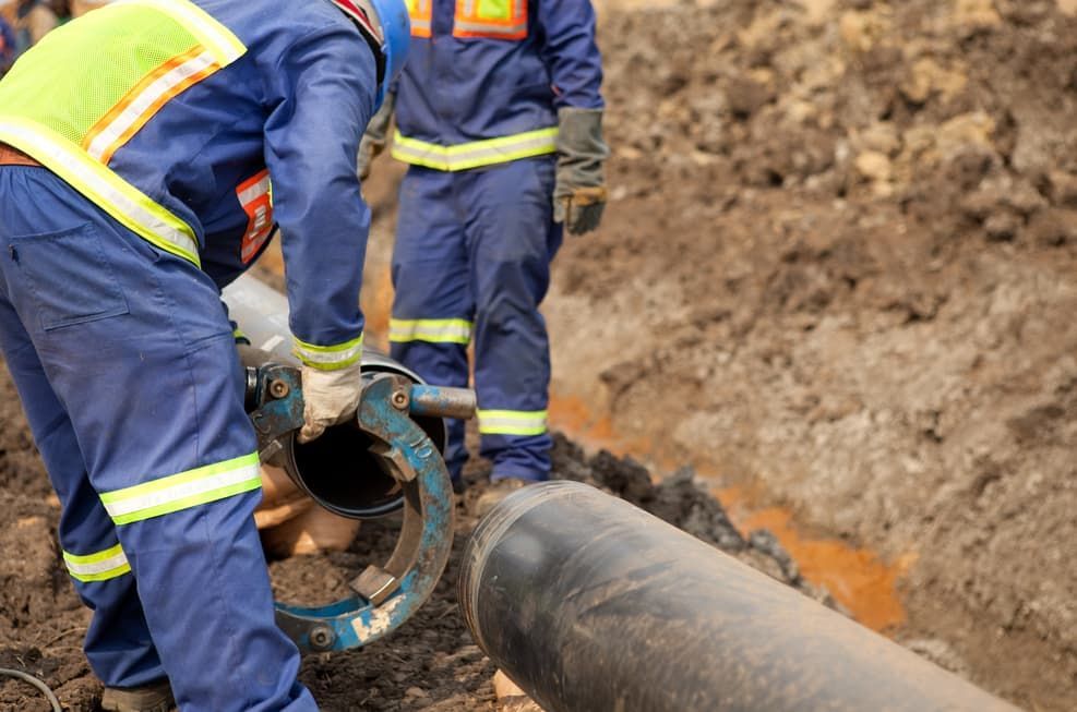A Group Of Construction Workers Are Working On A Pipe In The Dirt — JSB Plumbing & Gas In South Grafton, NSW