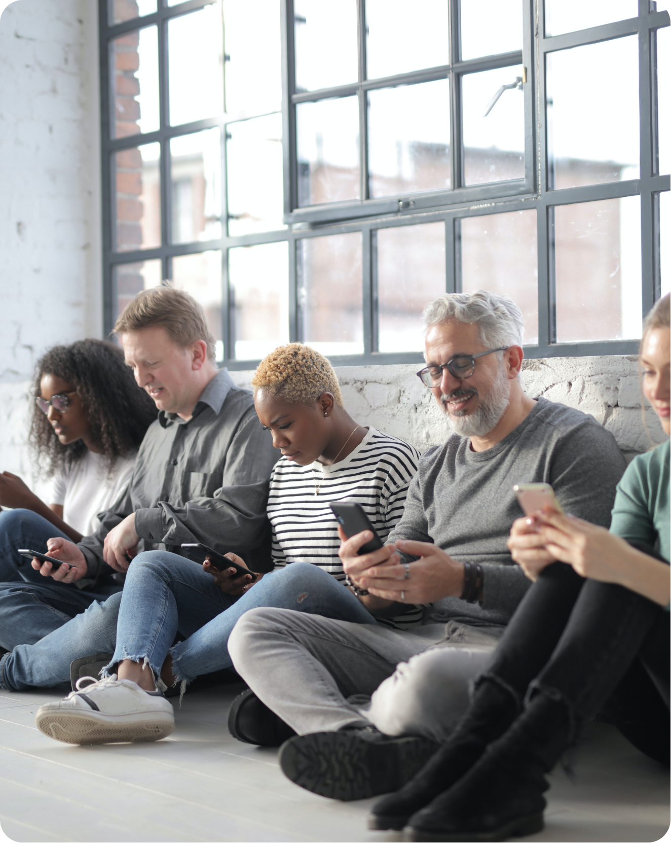 several people sitting on the floor against a wall and looking at their phones