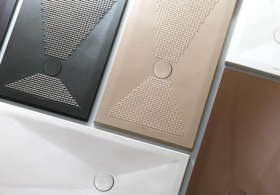 Su un tavolo sono disposti uno sopra l'altro tre piatti doccia di colore diverso.