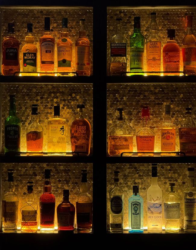 Illuminated bottles on backlit shelves in a dim bar or liquor display