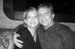 Couple smiling and embracing, indoors, woman with blonde hair, man with arm around her.