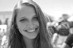 Smiling young woman with long hair, wearing hoop earrings. Outdoors, blurry background.