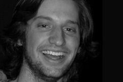 Man with long brown hair, smiling widely. Black and white photo.