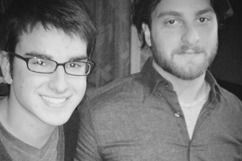 Two smiling men, one wearing glasses, pose closely for a photo.