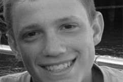 Smiling young man, fair skin, close-up, outdoors, boat railing in background.