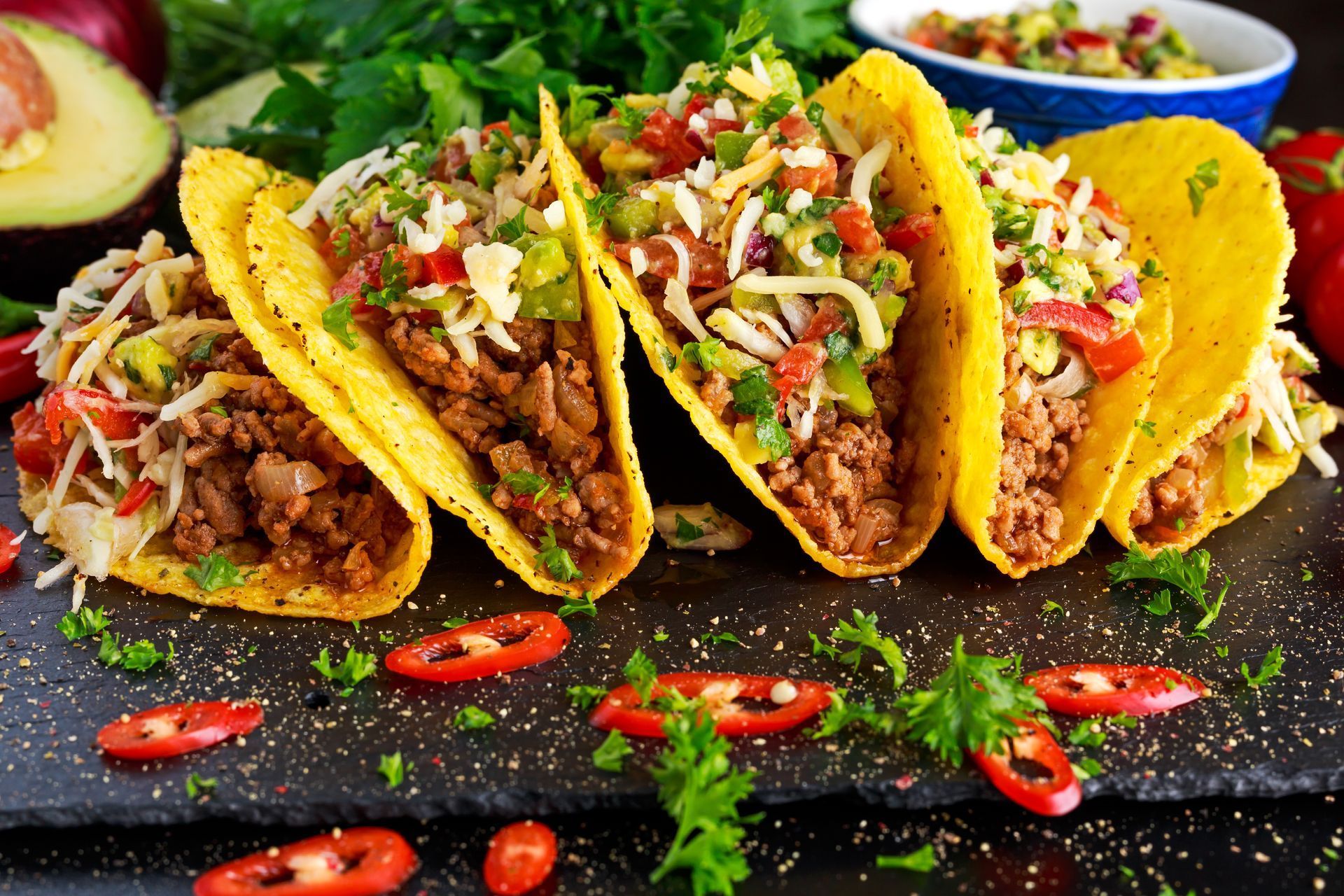A tray of tacos with meat , cheese , tomatoes and peppers on a table.