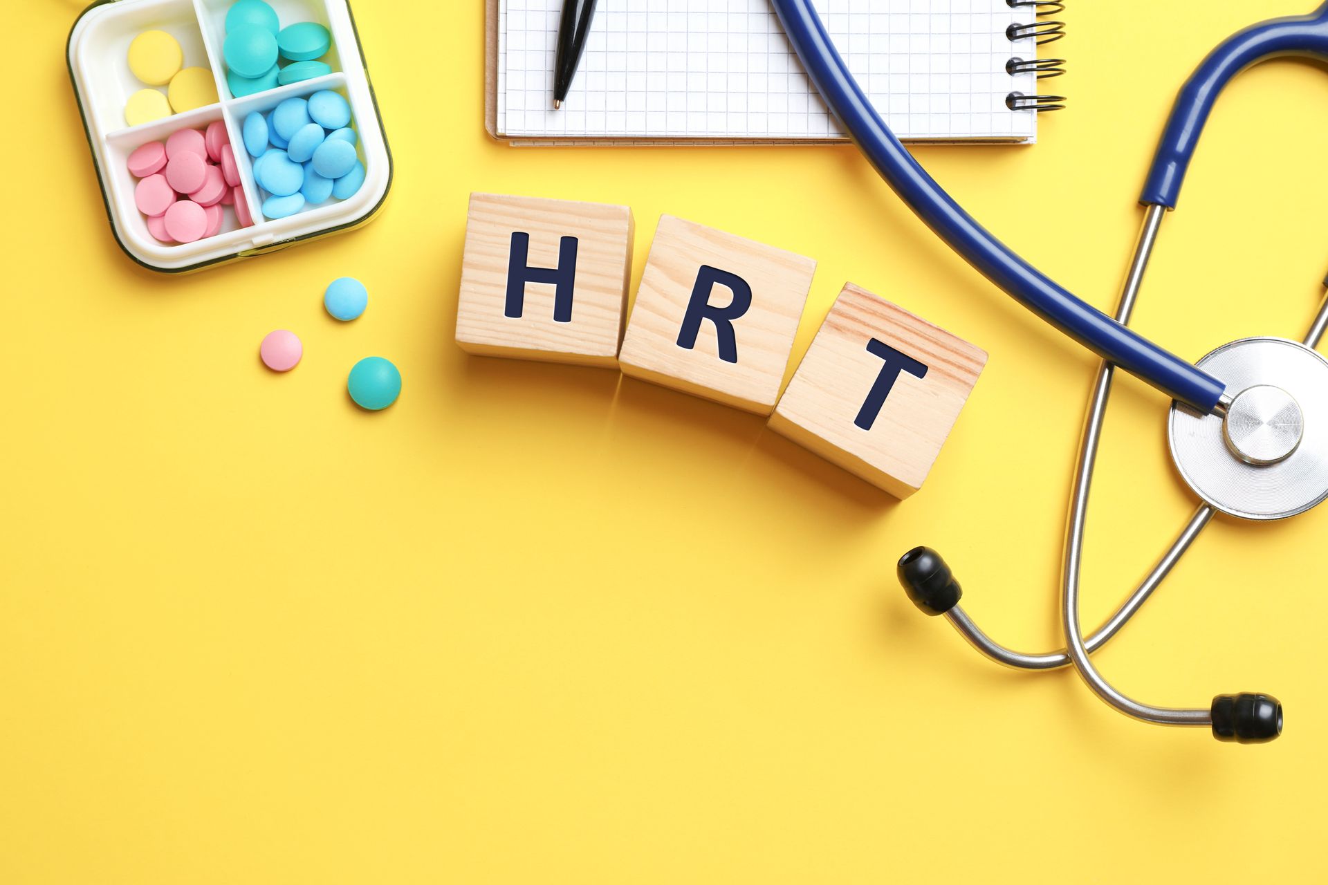 Wooden cubes with abbreviation HRT, pills, stethoscope and notebook on yellow background.