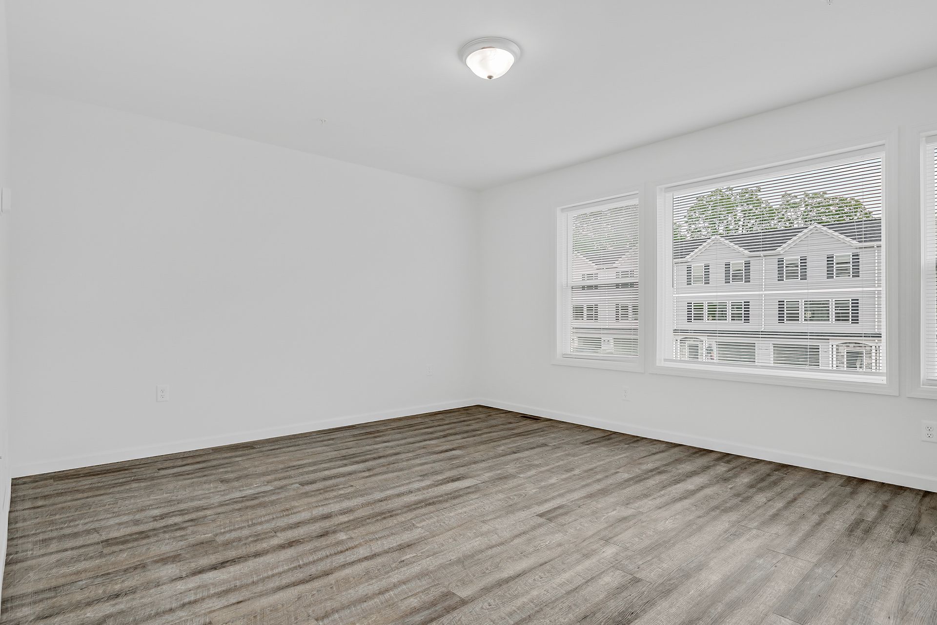 An empty room with hardwood floors and two windows.