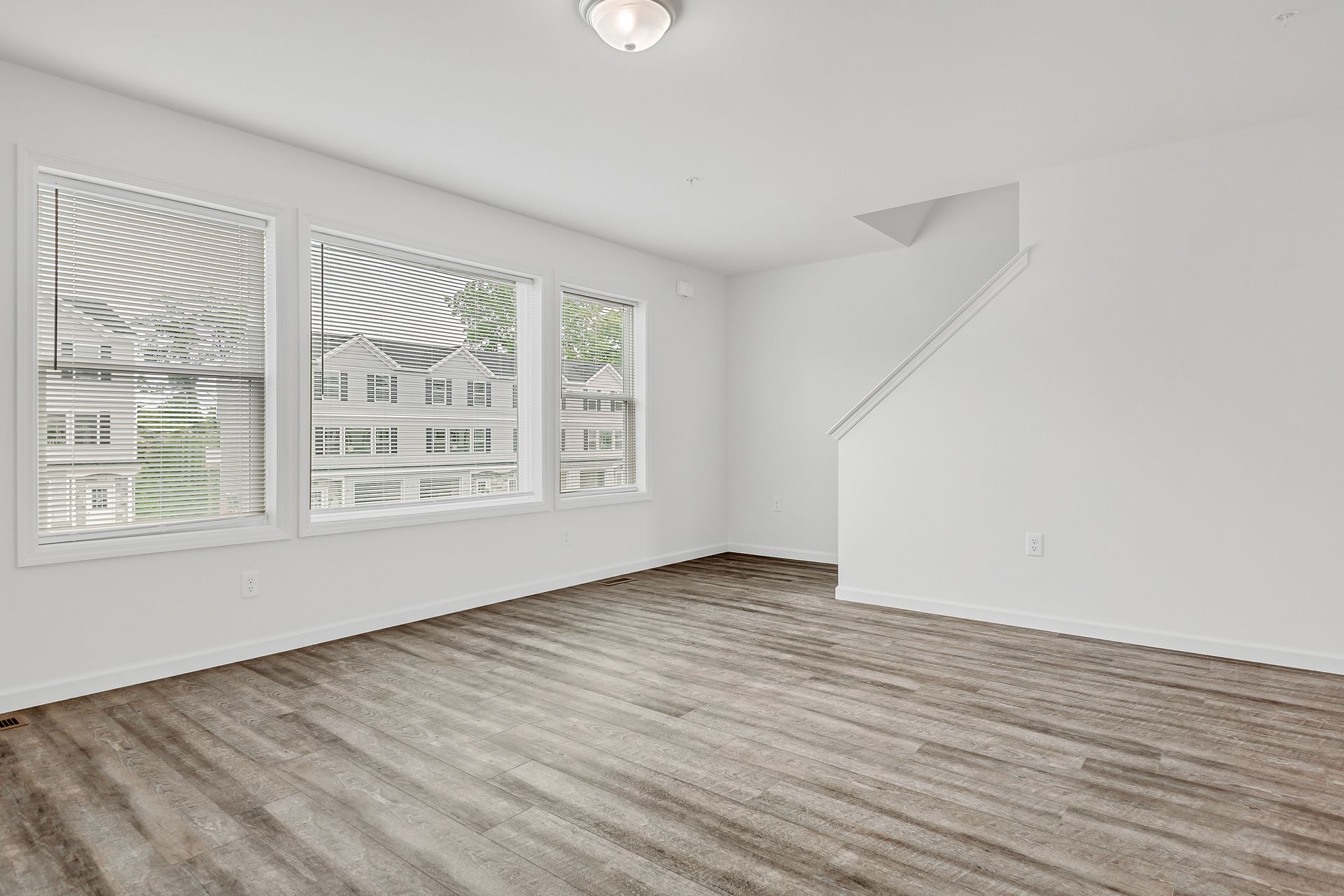 An empty living room with hardwood floors and lots of windows.