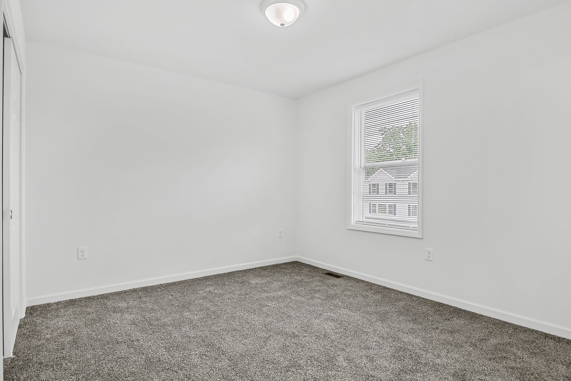 An empty bedroom with a window and a carpeted floor.