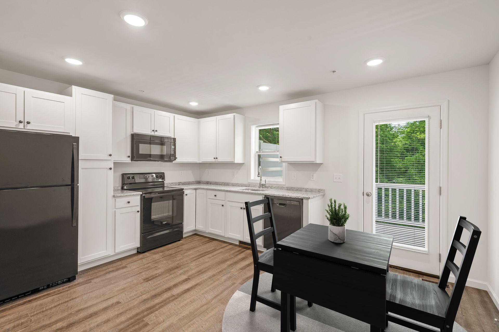 A kitchen with white cabinets , black appliances , a table and chairs.