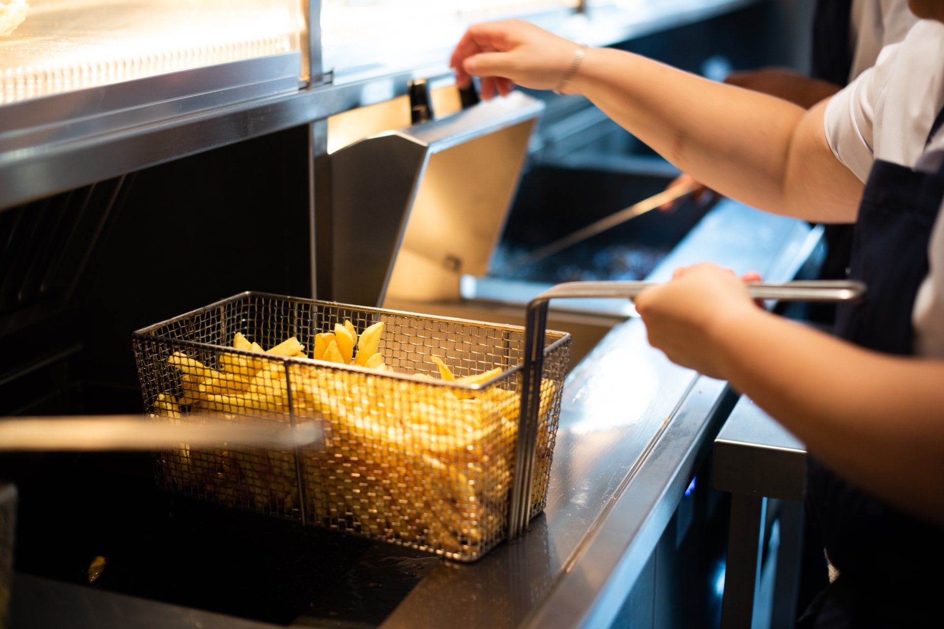 A person is cooking french fries in a fryer.